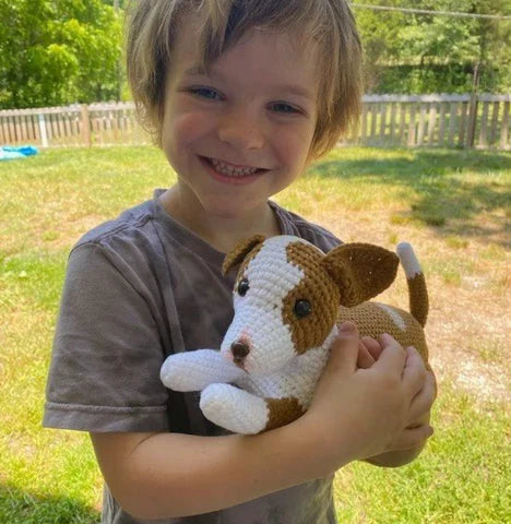 Child holding a stuffed dog toy outdoors on a grassy area